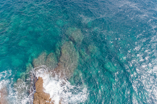 A bird's-eye view of how turquoise waves beat about sea cliffs in Montenegro