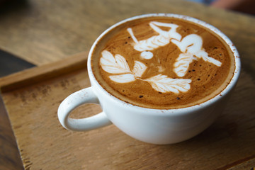 Close up of latte art coffee in a transparent glass on the wooden plate.