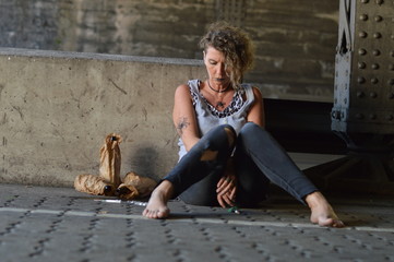 a hopeless punk woman under a bridge with bottles of alcohol and other drugs around her 