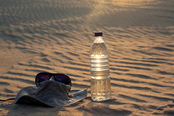 water bottle, hat and sunglasses lying on the sand in the desert