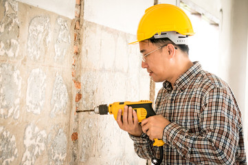 Foreman wearing helmet drilling wal by drill