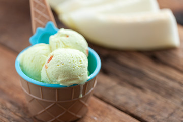 Vanilla ice cream with a taste of melon in a bowl on old wooden table. On the background of sliced fresh melon