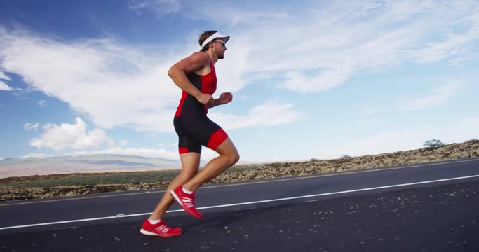 Triathlete running in triathlon suit training for ironman. Male runner exercising running uphill on road Big Island Hawaii. RED EPIC SLOW MOTION.