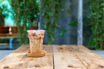 iced latte coffee in transparent plastic cup with black straw in coaster on the vintage wooden table with copy space for text. coffee concept.