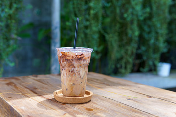 iced latte coffee in transparent plastic cup with black straw in coaster on the vintage wooden table with copy space for text. coffee concept.