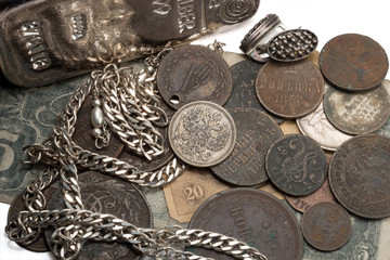 Antique silver, bullion and silver and bronze coins and jewelry lying on old banknotes. On the white background.
