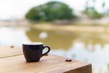 espresso or ristretto coffee in dark blue cup on the wooden table near the river in sunny day.