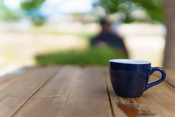 espresso or ristretto coffee in dark blue cup on the wooden table near the river in sunny day.