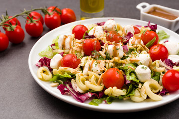 Healthy vegetarian mozzarella, cherry tomato and pasta salad with balsamic vinegar dressing and chopped almonds on a black stone background. Selective focus.