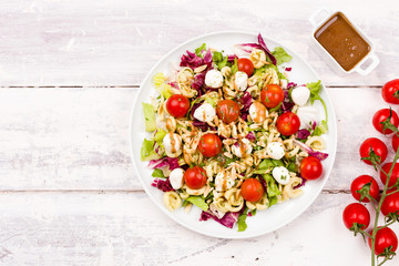 Top view of a healthy vegetarian mozzarella, cherry tomato and pasta salad with balsamic vinegar dressing and chopped almonds on a white wooden background. Diet food. Space for copy text.
