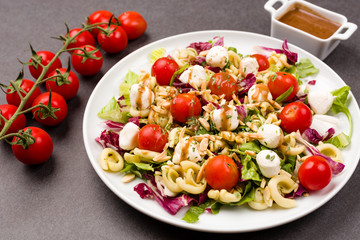 Healthy vegetarian mozzarella, cherry tomato and pasta salad with balsamic vinegar dressing and chopped almonds on a black stone background. Selective focus.