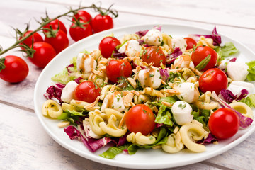 Healthy vegetarian mozzarella, cherry tomato and pasta salad with balsamic vinegar dressing and chopped almonds on a white wood background. Selective focus.