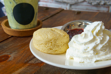 dessert scone with whip cream and strawberry jam with iced matcha green tea on the wooden table.