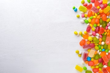 Colored candies, sweets and lollipops. On a white wooden background. Top view. Free space.