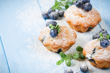Homemade baked muffin with blueberries, fresh berries, mint, powdered sugar on blue wooden background. Top view.