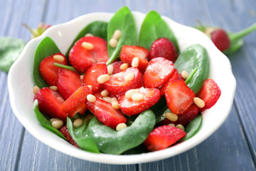 Plate of salad with spinach, strawberry and pine nuts on table