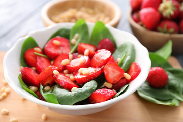 Plate of salad with spinach, strawberry and pine nuts on board