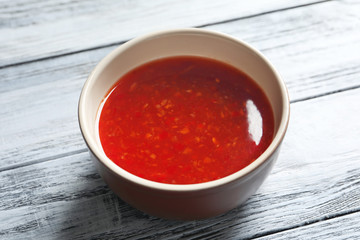 Ceramic bowl with chili sauce on wooden background