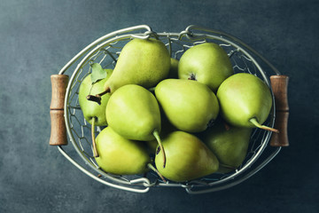 Ripe pears in metal basket on grey background