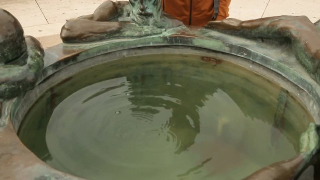 Male tourist throwing coin into fountain Well of Life in Zagreb city, tourism