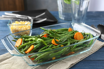 Delicious green beans and carrot slices in glass baking dish on table