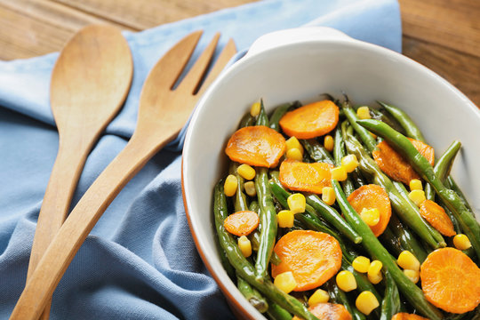 Casserole dish with delicious green beans, corn and carrot slices on fabric