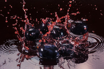 Fototapeta na wymiar Red juice or wine splash with grape berry closeup.