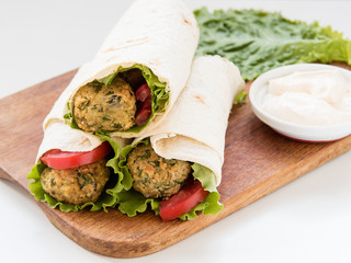 Falafel and fresh vegetables rolled in pita bread on wooden board