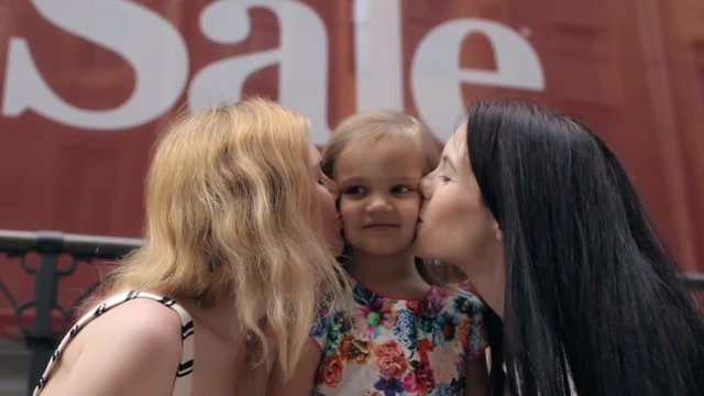 Two Happy Women Kiss a Little Girl, Daughter on a Background Inscription Sale
