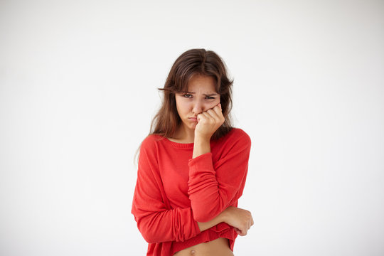 Unhappy stressed teenage girl with dark hair pressing her bruised cheek with painful expression, suffering from terrible toothache. Brunette woman having severe tooth pain, posing in studio