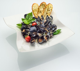 Top view and Close up of steamed clams with white wine, butter and garlic in a bowl. Garnished with lemon, parsley and bread slices. Served with a glass of white wine.