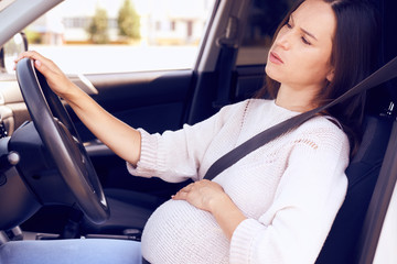 Young pregnant woman behind the steering wheel feeling bad
