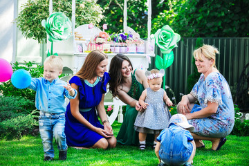 moms with their children playing on the grass in the yard against the backdrop of a candy bar at a children's party