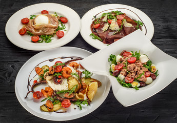 several types of the Italian salads on white plates over dark wooden background