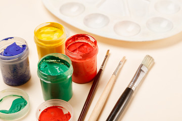 Paintbrushes, open paint jars and palette on a table, side view, copy space