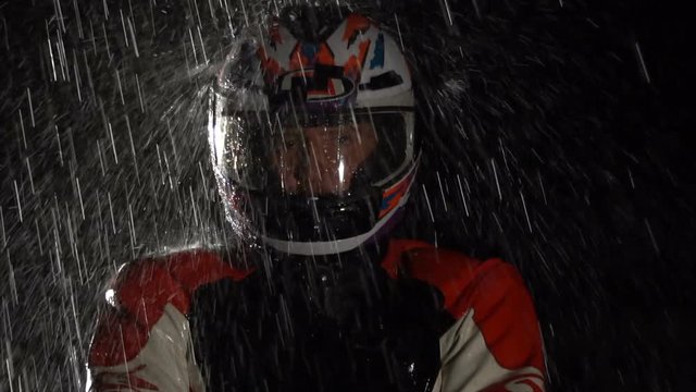 Racer in helmet standing in the rain at night. 