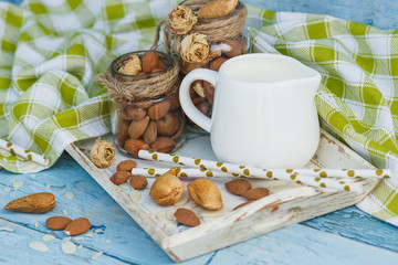 Almonds in the glass, jar with milk on the wooden tray and decorative tubes for drink