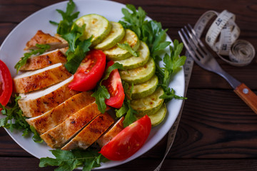 Diet concept, healthy lifestyle, low calorie food.  Baked chicken breasts with zucchini and salad with measuring tape on the table