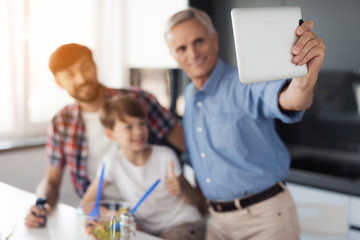 A man in a blue shirt makes selfie in the kitchen with his grandson and son. They are smiling