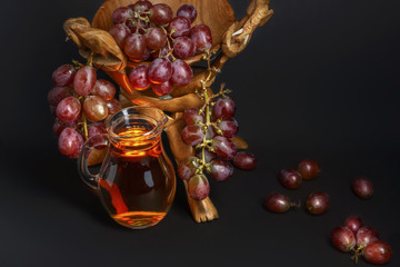 Glass jug with a drink of grapes surrounded by grapes on a beautiful antique bowl for fruit