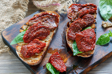 Board with toasted bread, sun dried tomatoes and basil.