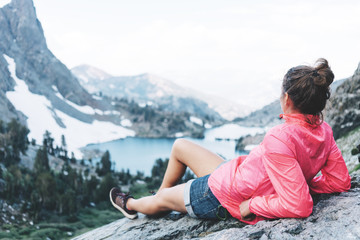 Naklejka na ściany i meble Handsome woman resting high in mountains. Risky rock climbing in peaceful wilderness area. Enjoying amazing snowy lake view