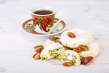 Traditional Iranian and Persian pieces of white nougat dessert sweet candies (Gaz) with Pistachio nuts from Isfahan City and a cup of tea on white wooden background