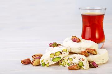 Traditional Iranian and Persian pieces of white nougat dessert sweet candies (Gaz) with Pistachio nuts from Isfahan City and a cup of tea on white wooden background