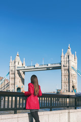 Naklejka premium Ludzie w Londynie styl życia miasto kobieta turystycznych patrząc na widok Tower Bridge w czerwonym płaszczu. Most. Stylowa elegancka dama moda dziewczyna spaceru ciesząc się miejskiego nowoczesnego życia.