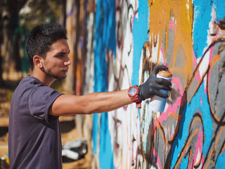 Fototapeta na wymiar Handsome Talented Young Boy making a colorful graffiti with aerosol spray on urban street wall. Cinematic tonedshot. Creative art. Side view