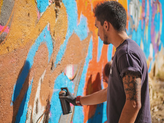 Obraz na płótnie Canvas Handsome Talented Young Boy making a colorful graffiti with aerosol spray on urban street wall. Cinematic tonedshot. Creative art. Side view