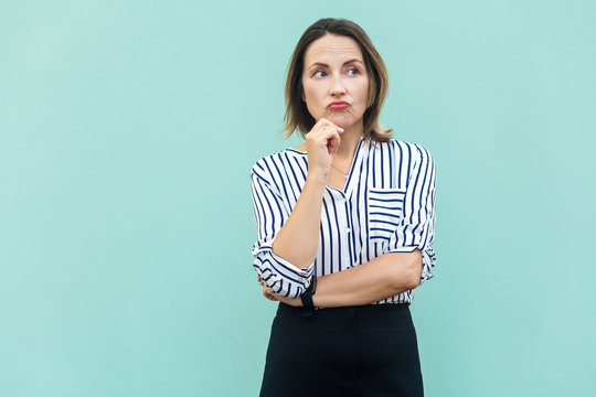 Thoughtful business woman looking away while standing against light blue wall.