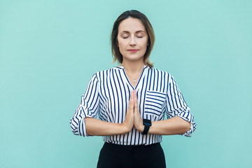 Meditation, religion and spiritual practises. Beautiful business woman doing yoga indoors at light blue wall, keeping eyes closed, holding fingers in mudra gesture.