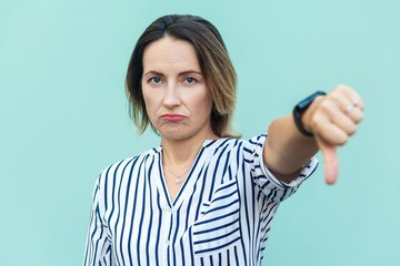 Portrait of unsatisfied sensual lady with thumbs down and white shirt against light blue background.
